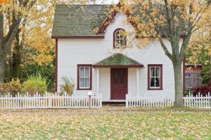 two floor home with a white picket fence during fall